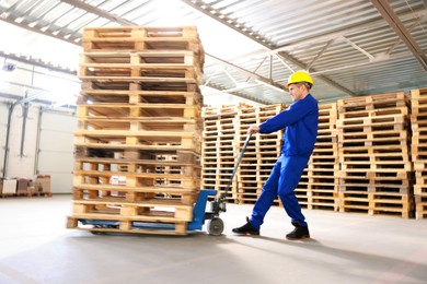 Image of Worker moving wooden pallets with manual forklift in warehouse