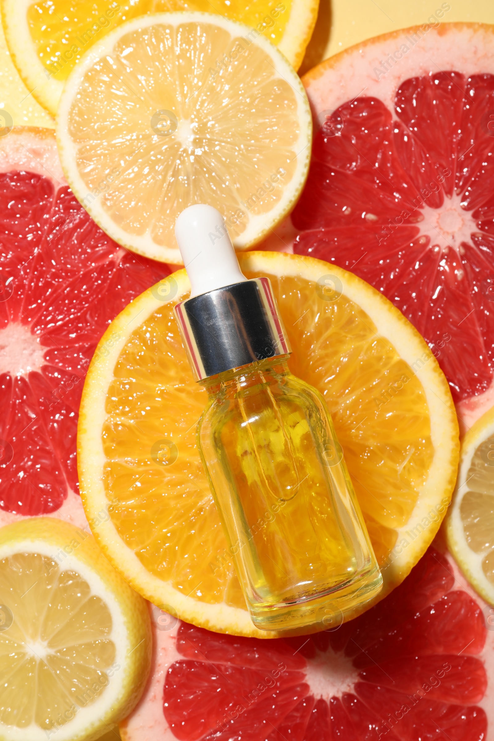 Photo of Bottle of cosmetic serum and sliced citrus fruits on yellow background, flat lay