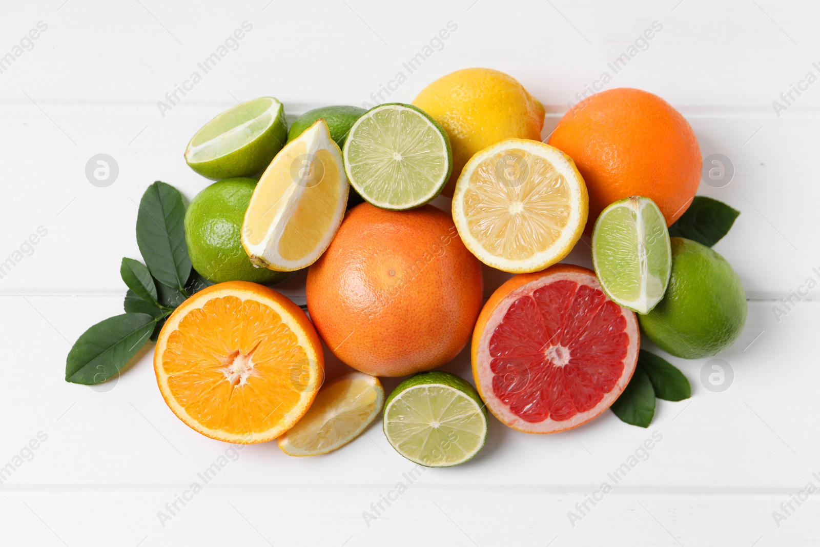 Photo of Different fresh citrus fruits and leaves on white wooden table, flat lay