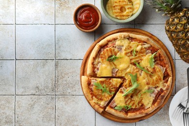 Photo of Delicious cut pineapple pizza and ingredients on light gray tiled table, flat lay. Space for text