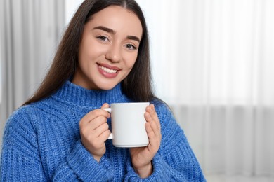 Photo of Happy young woman holding white ceramic mug at home, space for text