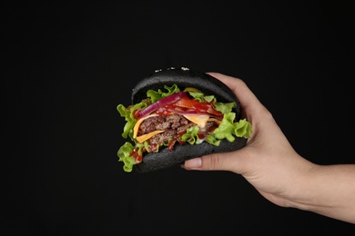 Photo of Woman holding black burger against dark background, closeup