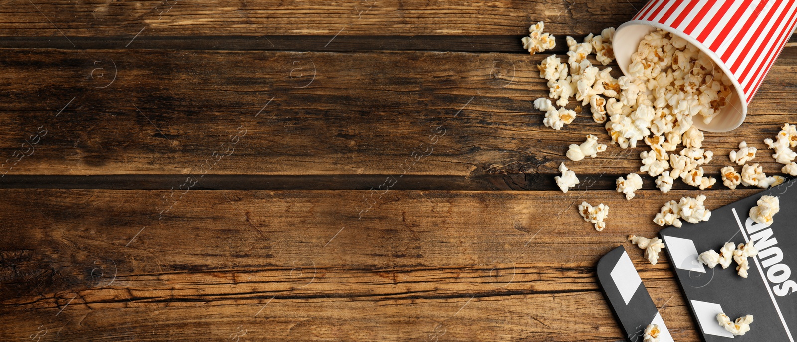 Image of Tasty fresh popcorn and clapboard on wooden table, flat lay with space for text. Banner design