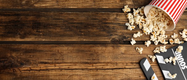 Image of Tasty fresh popcorn and clapboard on wooden table, flat lay with space for text. Banner design