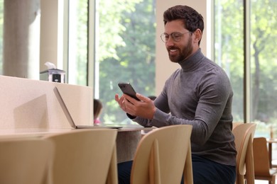 Photo of Handsome man using smartphone at table in cafe