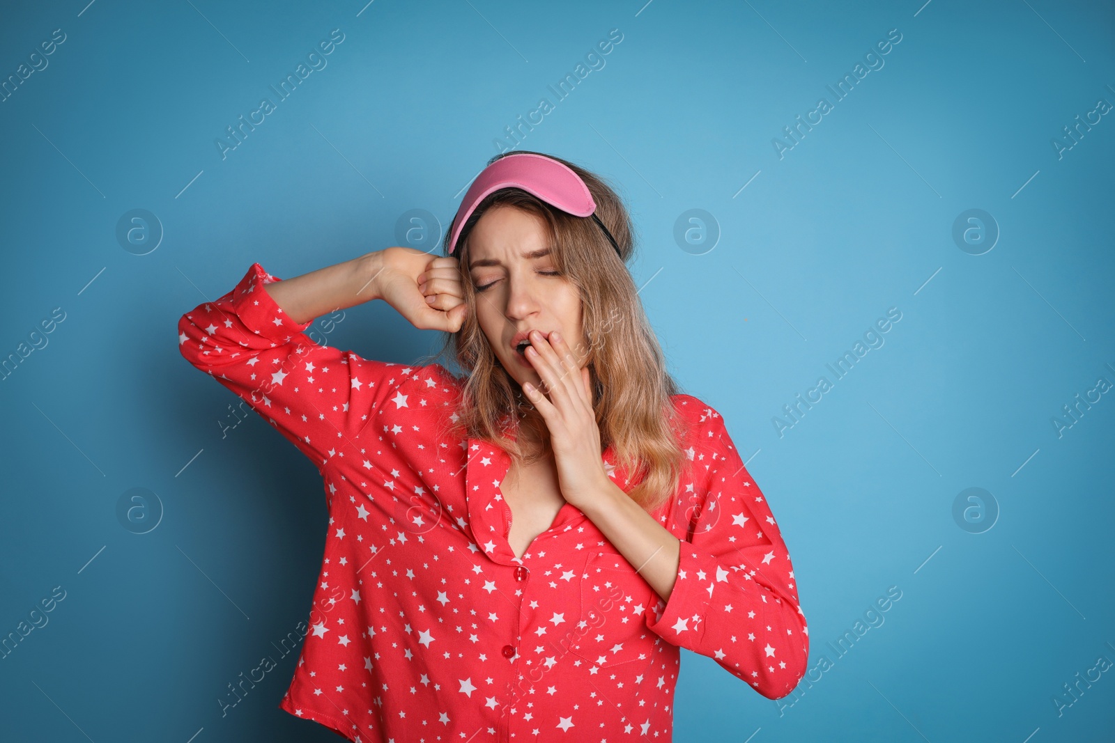 Photo of Young tired woman with sleeping mask yawning on light blue background