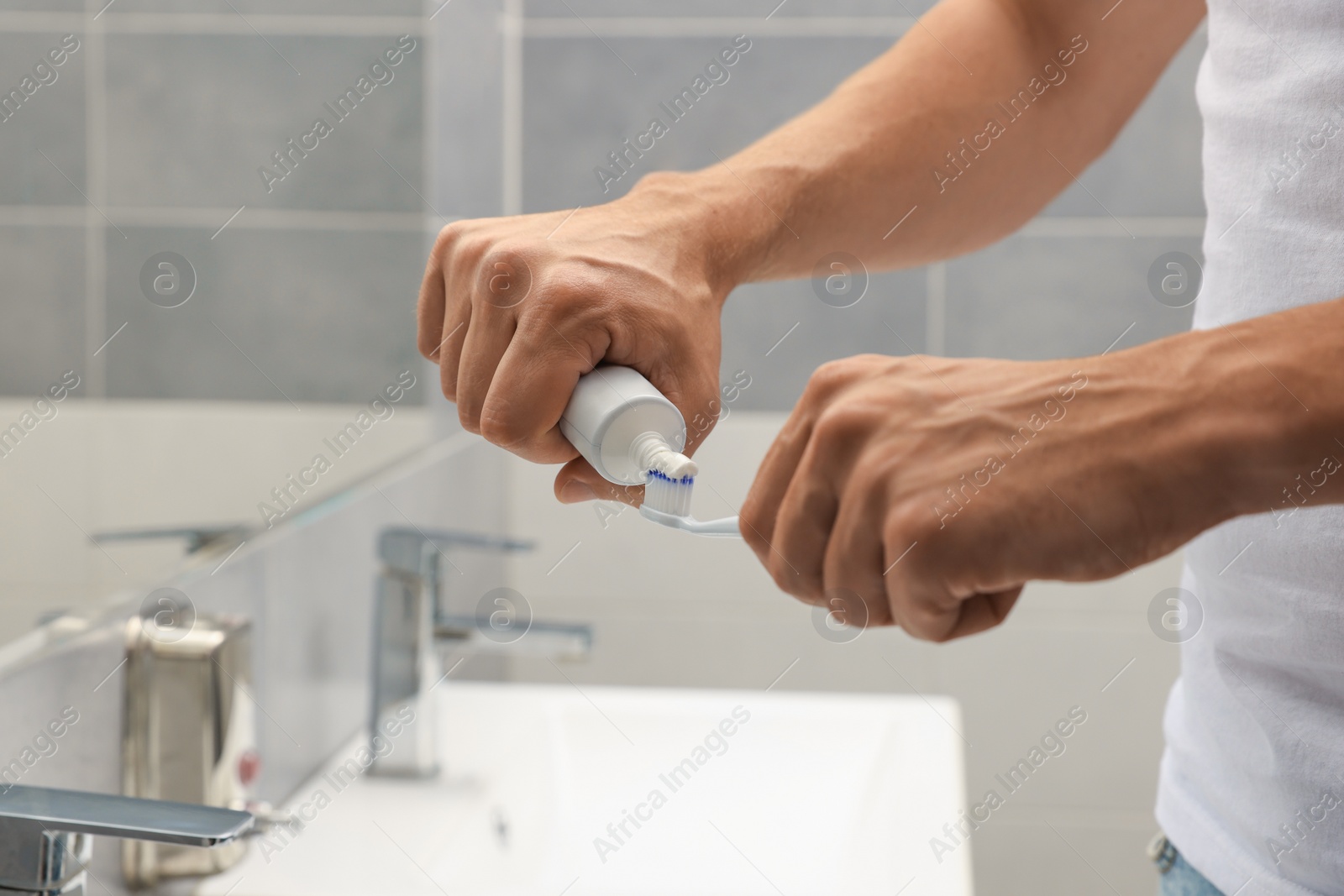 Photo of Man applying toothpaste on brush in bathroom, closeup