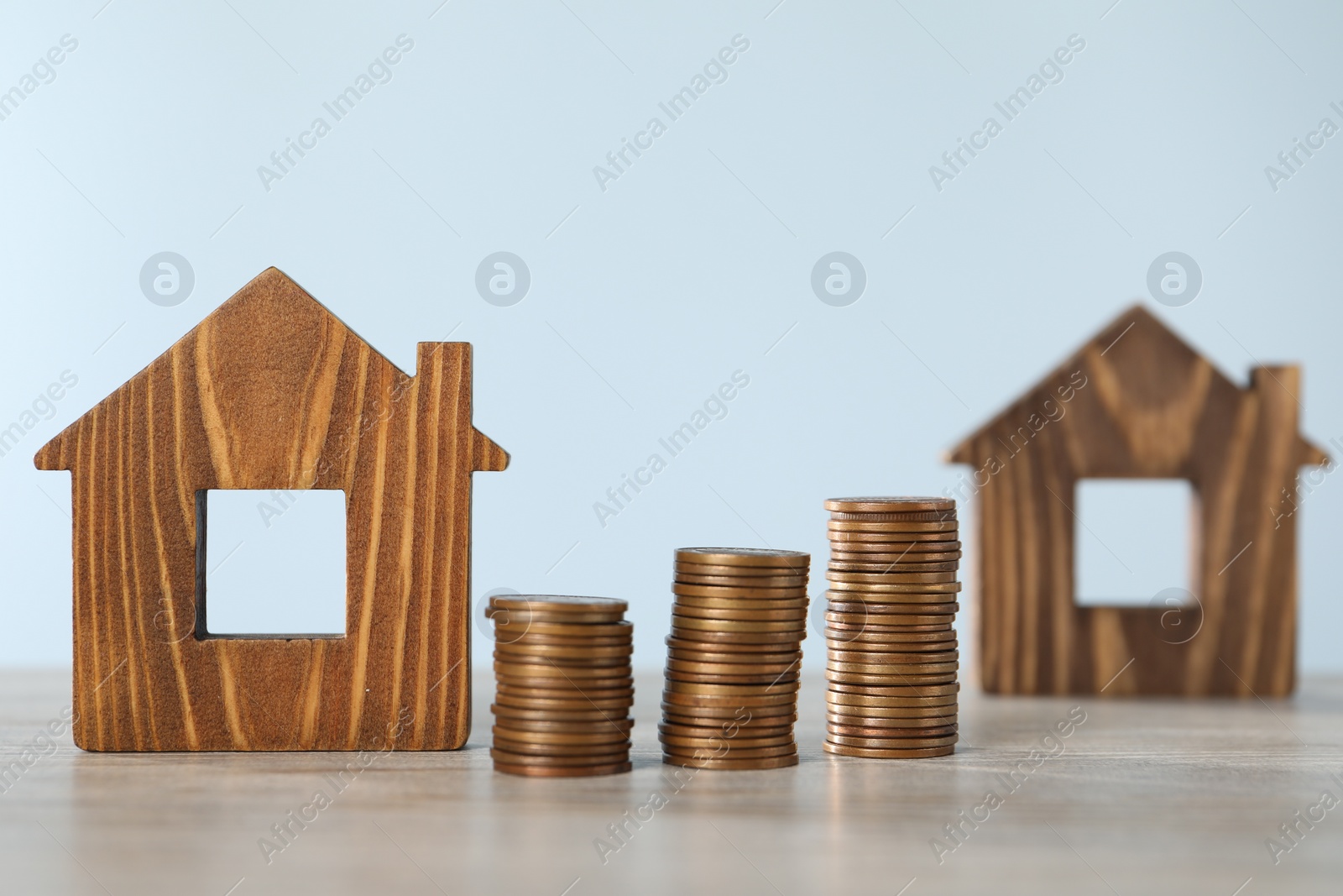 Photo of House models and stacked coins on wooden table against light blue background