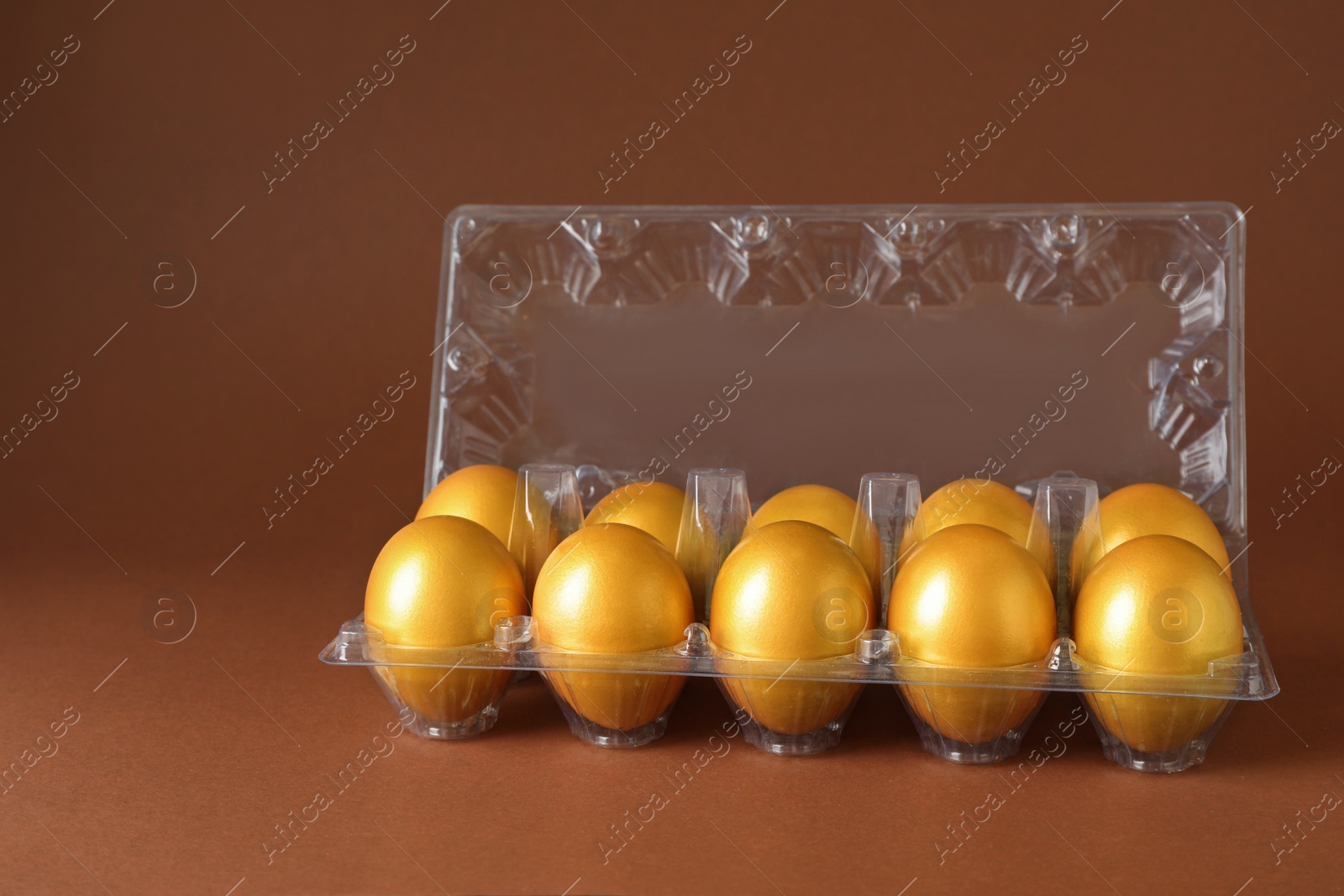 Photo of Shiny golden eggs in plastic box on brown background