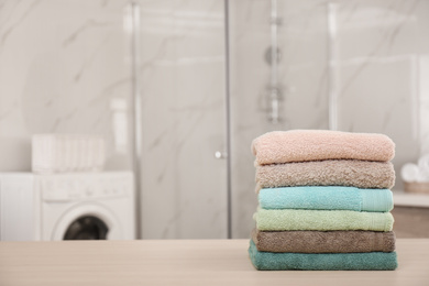 Photo of Stack of fresh towels on wooden table in bathroom. Space for text