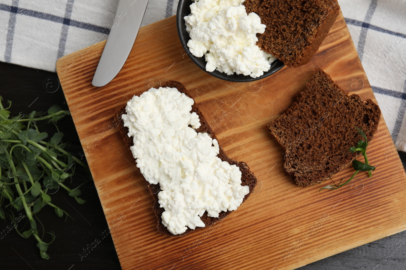 Photo of Bread with cottage cheese and microgreens on black wooden table, flat lay