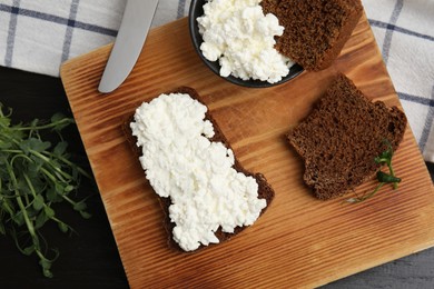 Bread with cottage cheese and microgreens on black wooden table, flat lay