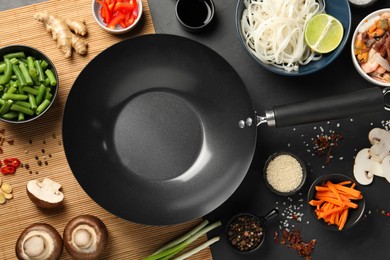 Flat lay composition with black wok, spices and products on dark table