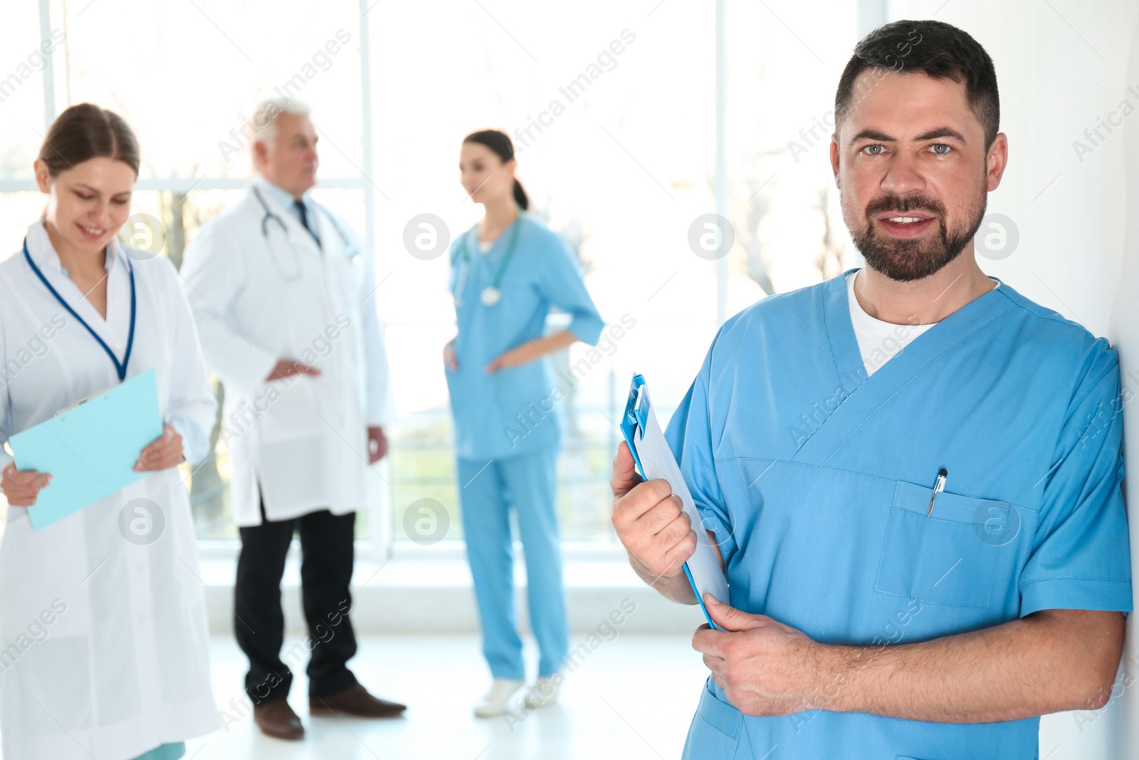 Photo of Mature doctor with clipboard and colleagues in hospital. Medical service