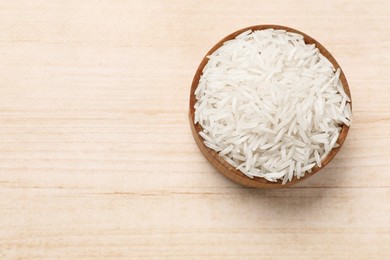 Photo of Raw basmati rice in bowl on white wooden table, top view. Space for text