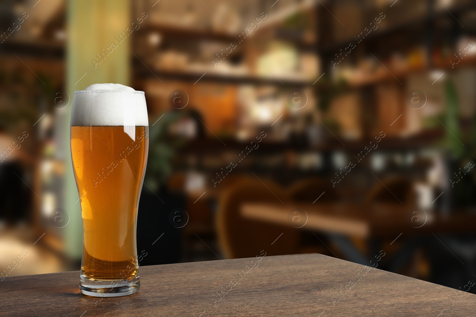 Image of Glass with fresh beer on wooden table in pub, space for text