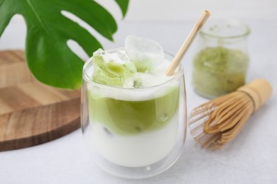 Glass of tasty iced matcha latte, leaf and bamboo whisk on white table, closeup