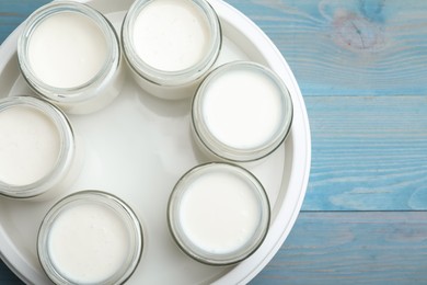 Modern yogurt maker with full jars on blue wooden table, flat lay