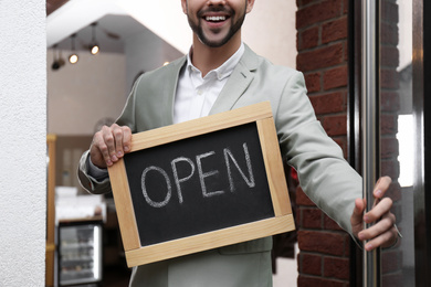 Young business owner holding sign OPEN at door of his cafe, closeup