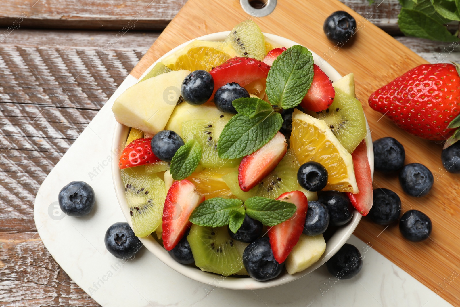 Photo of Tasty fruit salad in bowl and ingredients on wooden table, flat lay