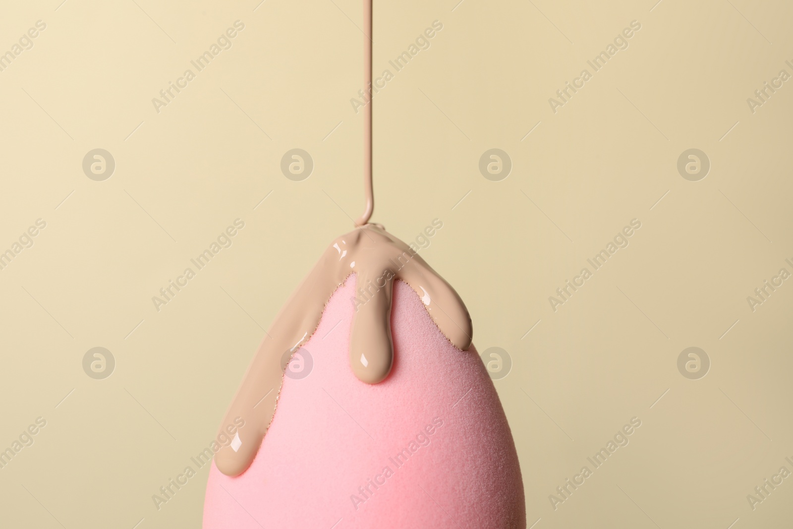 Photo of Skin foundation pouring onto makeup sponge on beige background