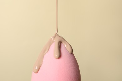 Photo of Skin foundation pouring onto makeup sponge on beige background