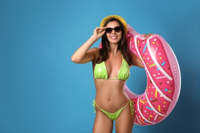 Beautiful woman in stylish bikini with inflatable ring on blue background. Space for text