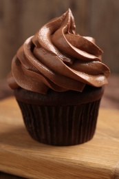 Photo of Delicious chocolate cupcake with cream on wooden board, closeup