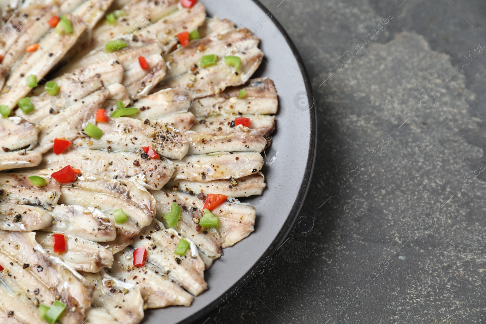 Photo of Tasty pickled anchovies with spices on grey textured table, closeup. Space for text