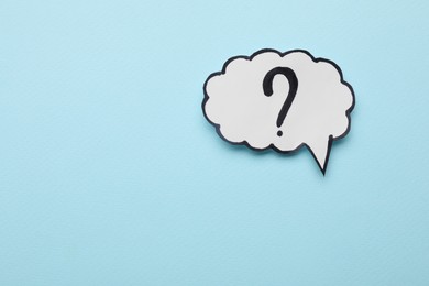 Paper speech bubble with question mark on light blue background, top view. Space for text