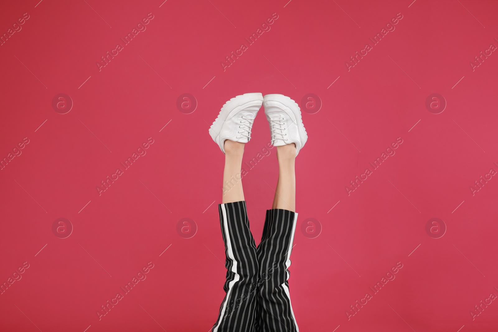 Photo of Woman in stylish sport shoes on crimson background