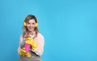 Photo of Beautiful young woman with headphones and bottle of detergent singing on light blue background. Space for text