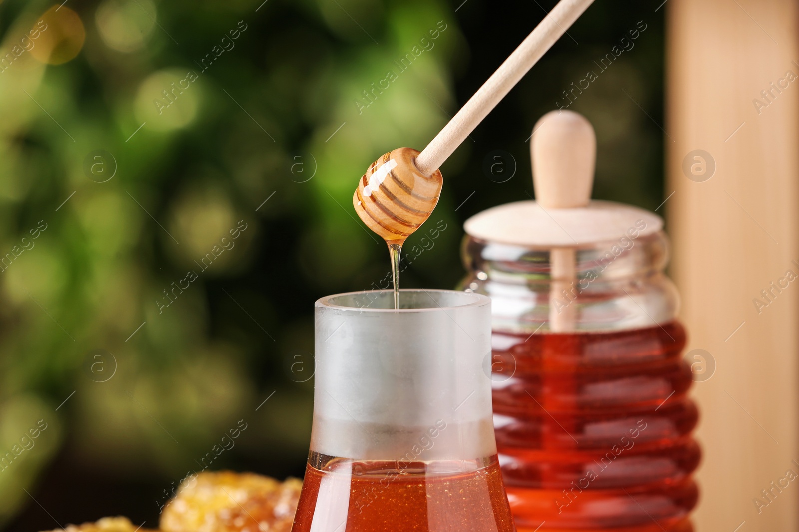 Photo of Dripping tasty honey from dipper into jar on green blurred background