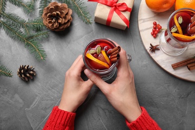 Young woman holding glass of tasty mulled wine at grey table, top view