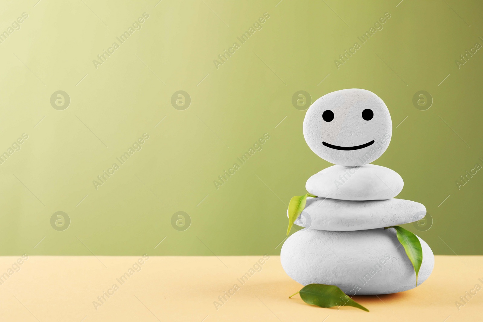 Photo of Stack of stones with drawn happy face and leaves on beige table against light green background, space for text. Zen concept