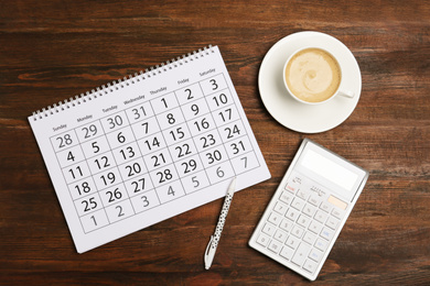 Photo of Flat lay composition with calendar and cup of coffee on wooden table