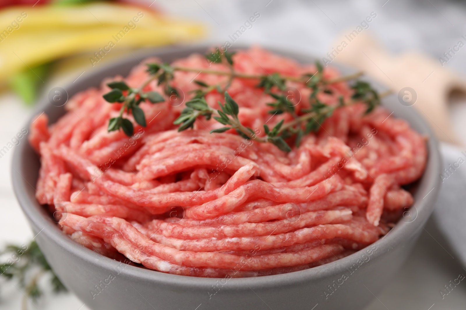 Photo of Fresh raw ground meat and thyme in bowl on table, closeup