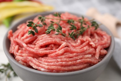 Fresh raw ground meat and thyme in bowl on table, closeup