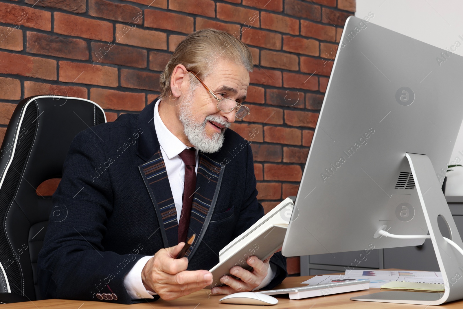 Photo of Happy senior boss having online meeting via computer at wooden table in office