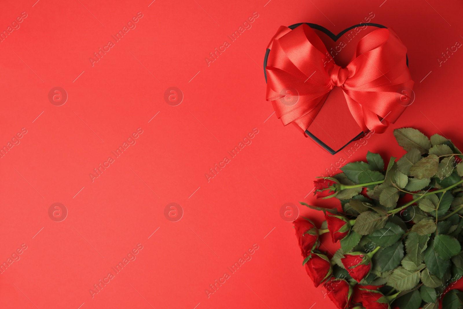 Photo of Heart shaped gift box with bow and beautiful roses on red background, flat lay. Space for text