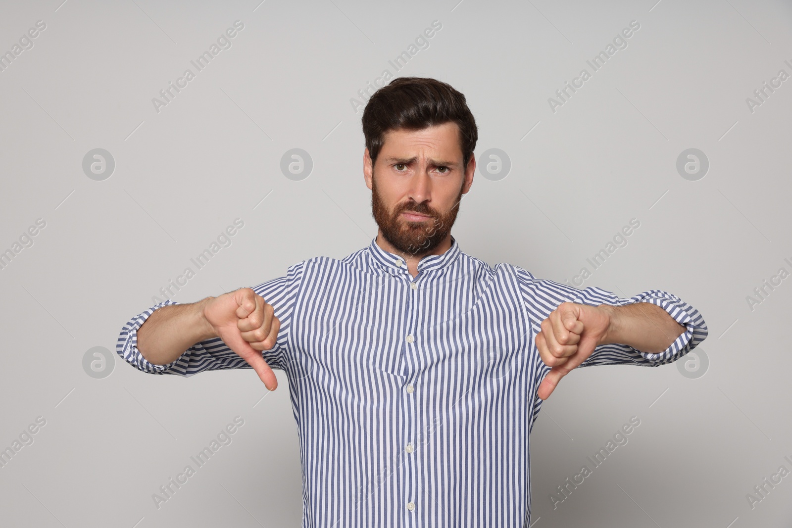 Photo of Handsome bearded man showing thumbs down on light grey background