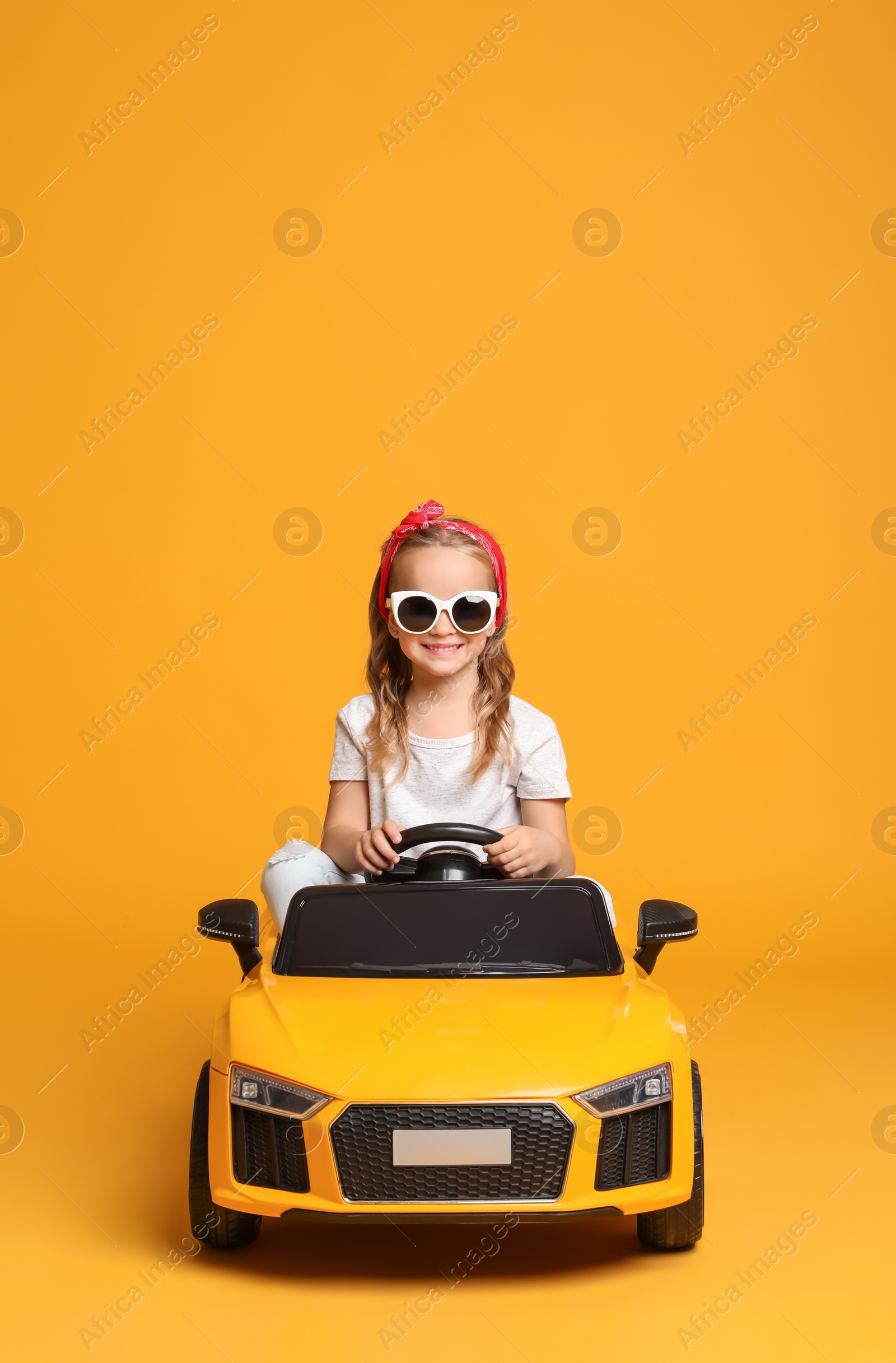 Photo of Cute little girl driving children's electric toy car on yellow background