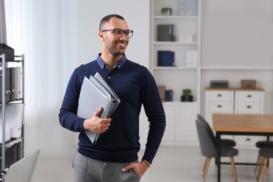 Photo of Smiling young businessman with folders in modern office. Space for text