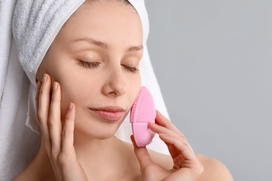 Photo of Washing face. Young woman with cleansing brush on grey background, closeup. Space for text