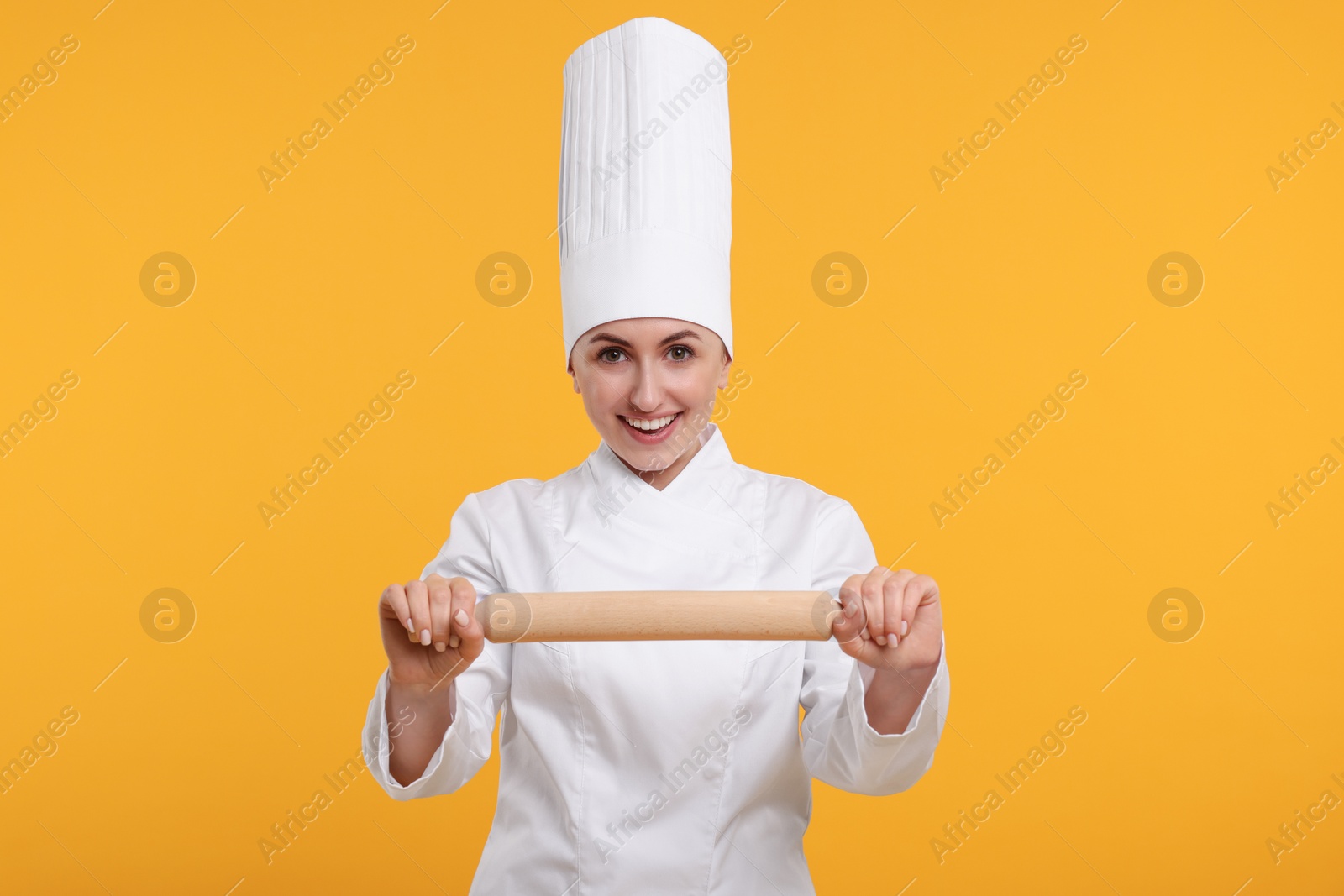 Photo of Happy professional confectioner in uniform holding rolling pin on yellow background