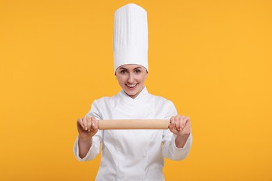 Photo of Happy professional confectioner in uniform holding rolling pin on yellow background