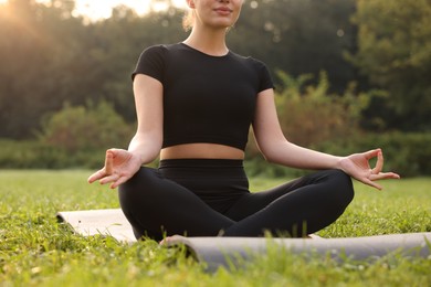 Woman practicing yoga on mat outdoors, closeup. Lotus pose