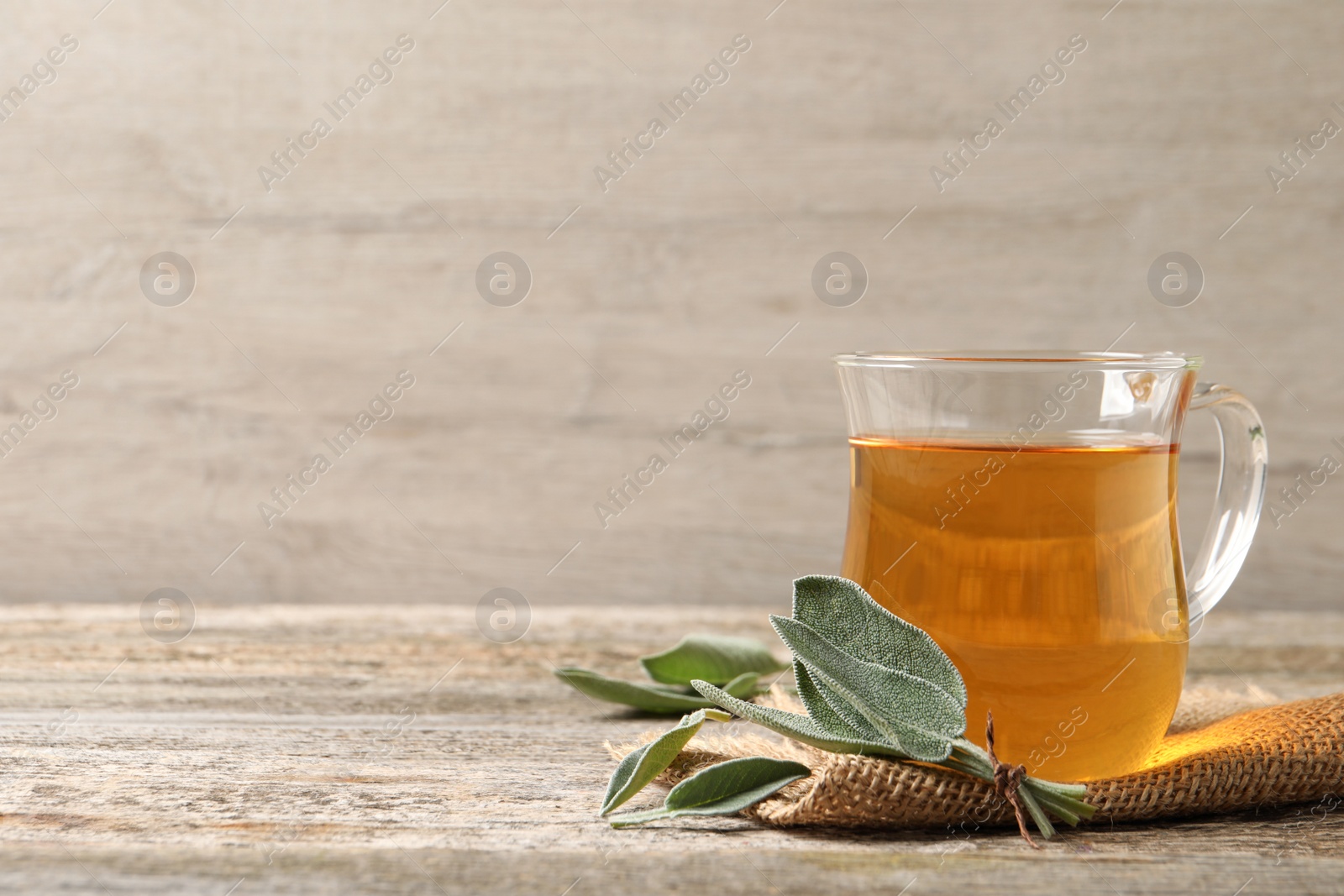 Photo of Cup of aromatic sage tea and fresh leaves on wooden table. Space for text