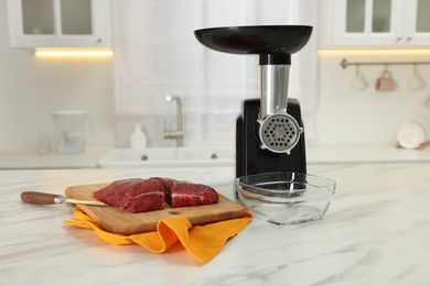 Photo of Electric meat grinder with beef and knife on white marble table in kitchen