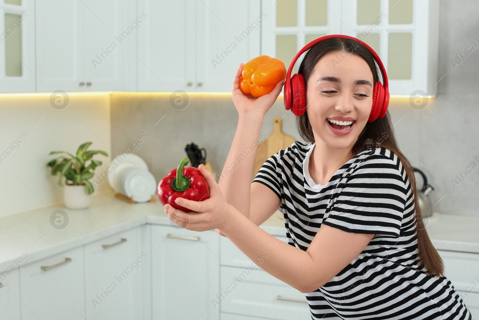 Photo of Happy woman in headphones listening music and dancing with bell peppers in kitchen. Space for text